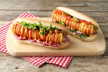 Tasty hot dogs with vegetables, mustard and ketchup on wooden table