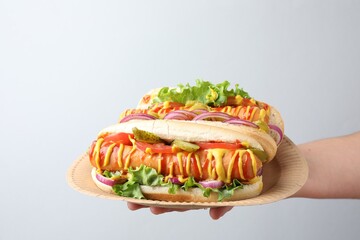 Woman with tasty hot dogs on light grey background, closeup