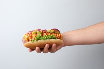 Woman with tasty hot dog on light grey background, closeup