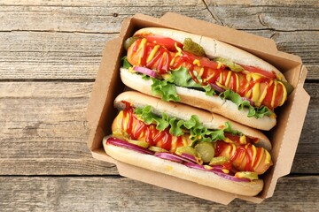Tasty hot dogs with vegetables, mustard and ketchup on wooden table, top view. Space for text
