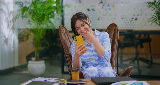 Afghan young adult gen z woman lady sitting on chair use mobile look cam talk gossip indoor job place happy girl staff hold phone speak on video call after work enjoy break spend day time at office