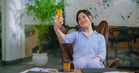 Happy young adult gen z woman lady hold mobile look came take selfie do pose enjoy day at job work...