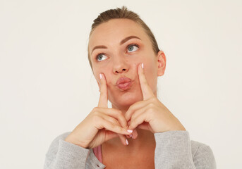 A cheerful young woman grimaces at the camera, presses her fingers to her cheeks, having fun....