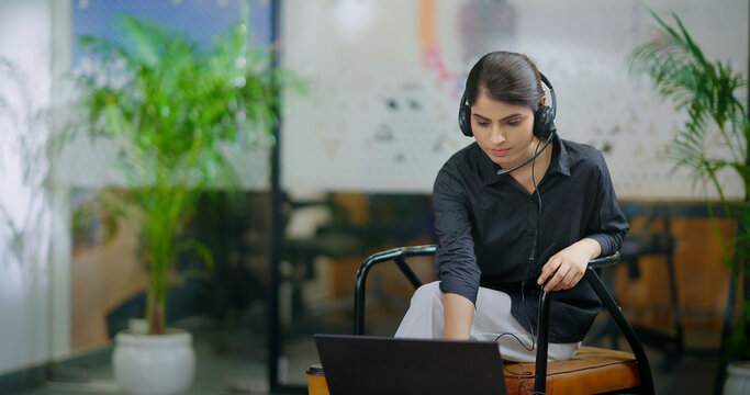 Indian Asian Hindu busy youth lady woman sitting chair use laptop talk speak client online video call indoor office young adult female girl staff worker agent do sales task job tele center look webcam