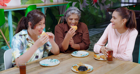 Indian happy senior woman lady group sitting around table eat break time tasty lunch share food pick up cup drink coffee work place female girl staff talk gossip enjoy day have fun joy job office
