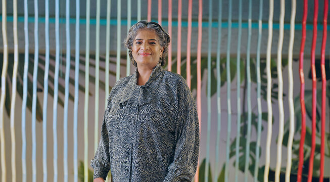 Indian happy old aged gray haired women boss lady leader ceo standing proud look camera indoor work place Asian alone older elder adult female staff staring cam do pose job office