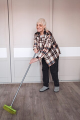 An elderly woman with a short haircut sweeps the room with a mop.