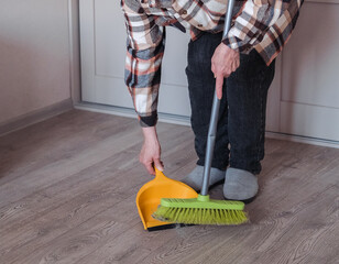An elderly woman wearing casual clothes is sweeping the room.