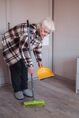 An elderly woman wearing casual clothes is sweeping the room.