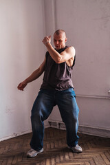 A forty year old sporty man in casual clothes dances in a room.
