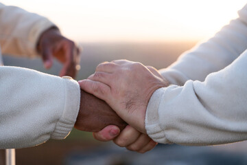 Two individuals clasping hands in a moment of connection during sunrise in an outdoor setting...