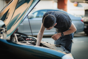 A young man looks inside the hood of a car.