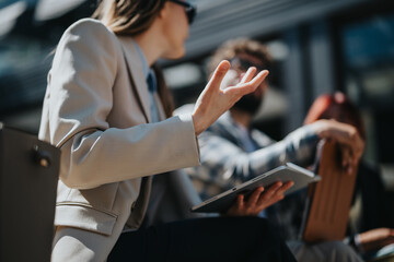 Business professionals collaborating, focusing on a discussion while using technology outdoors,...