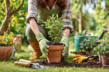 Beautiful young gardener planting a plant directly into the ground without a pot, using hands, full-body photo in a garden with tools like gloves and trowel on fresh earth