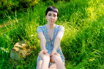 Young woman in floral dress relaxing on grass in a sunny outdoor setting, enjoying nature's beauty...
