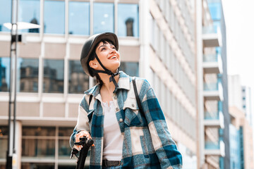 Young woman in a checkered jacket and helmet enjoying a sunny day while riding an electric scooter...