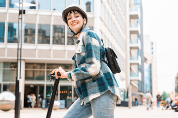 Young woman smiles while riding scooter on urban street surrounded by modern buildings during daytime