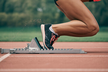 Close-up of female athlete in running shoes on starting block at running track. Concept of speed and competition