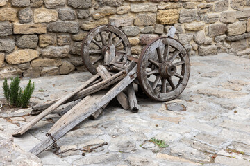 Rustic wooden cart wheels and a wooden chassis lean against a stone wall