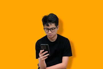 young man Wearing Glasses Using a Smartphone Against an Orange Background
