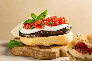 Sandwich with roasted eggplant, mozzarella di bufala cheese, tomatoes with basil leaves. Italian panino caprese. Beige background.
