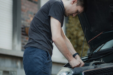 A young man unscrews a headlight bulb inside the hood.