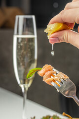 A delicate forkful of fresh salmon garnished with greens is drizzled with lemon juice, accompanied...