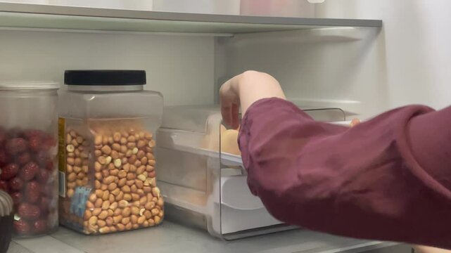A video shows the whole process: opening the fridge door, pulling out the egg - storage drawer, taking an egg, and closing the fridge. A simple daily kitchen task captured clearly.