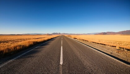 Naklejka premium empty cracked asphalt road stretching straight into the horizon under clear blue sky with golden fields and distant low mountains bathed in warm sunlight