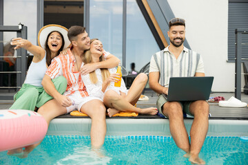A joyful group of friends relax by the pool while enjoying drinks and the summer sunshine, embodying carefree moments and friendship.