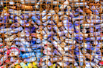 Variety of crushed cans collected in a mesh cage at a recycling facility on a sunny afternoon