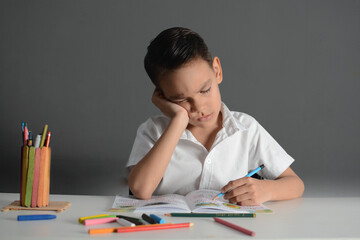 Frustrated young boy doing schoolwork with an angry expression, gripping a pencil tightly at his...