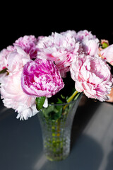 Beautiful peonies in a glass vase in bright sunlight.