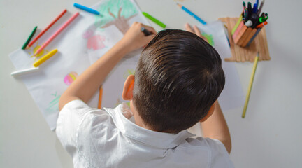  Top-down shot of a child drawing colorful shapes on paper, surrounded by school materials on a...