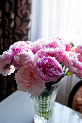 Beautiful peonies in a glass vase in bright sunlight.