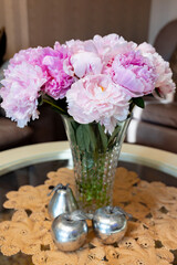 Beautiful peonies in a glass vase on a table with decorative silver fruits.