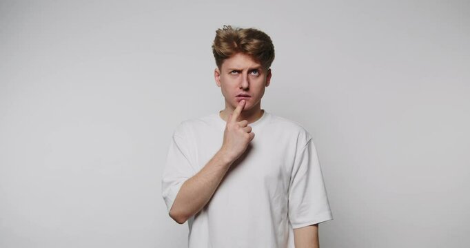 Young man pondering with curious expression in a minimal studio setting, capturing a moment of thought