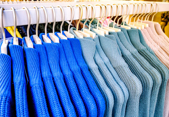 Hangars filled with various shades of blue knit sweaters in a retail store during daytime