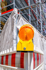 Construction zone barrier with warning light near scaffolding at a busy urban location during...