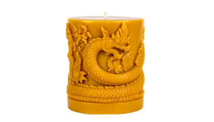 A cylindrical beeswax candle adorned with an intricately carved dragon design. The candle is a rich amber color, and the dragon is depicted in a dynamic pose. The scene is peaceful and serene.