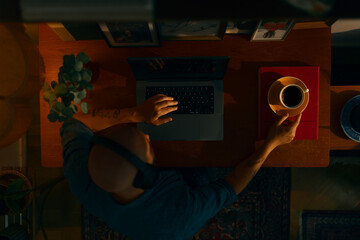 Portrait of a young caucasian man wearing wireless headphones using a laptop sitting in a cosy living room, top view.