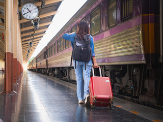 A young woman dragging a suitcase on a platform looks at her watch.