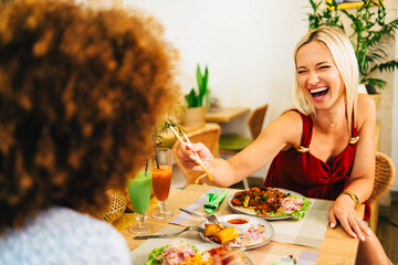 Two female friends enjoying lunch at restaurant with asian food and drinks
