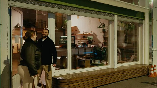 A female owner and a male employee leave a cafe and talk while she closes it