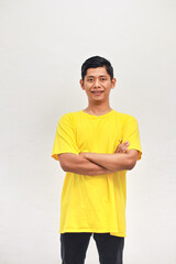 Portrait of a smiling Asian man in a yellow t-shirt with arms crossed on white background