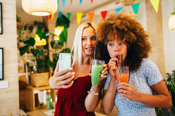 Two female friends taking a selfie while drinking smoothies in a restaurant