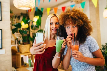 Fotobehang Two female friends taking a selfie while drinking smoothies in a restaurant © djile
