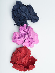 Three crumpled pieces of paper in varying colors: dark blue, light pink, and red.