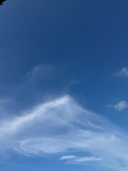 A clear, vibrant blue sky adorned with delicate, wispy cirrus clouds forming abstract patterns.