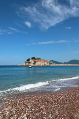 View from the beach on the left side of Sveti Stefan Island, Montenegro. Waves of the Adriatic Sea, clean sandy beach. Budva Municipality